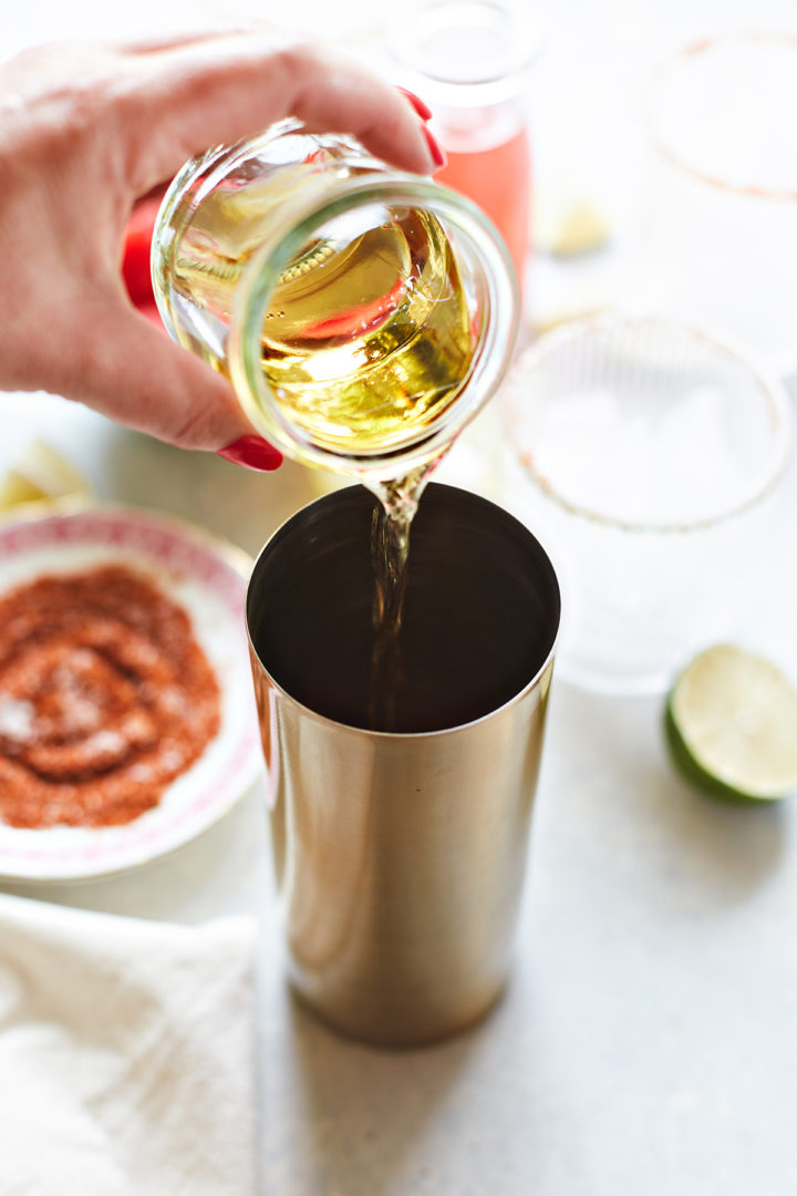 woman adding tequila to a cocktail shaker to make a watermelon margarita recipe