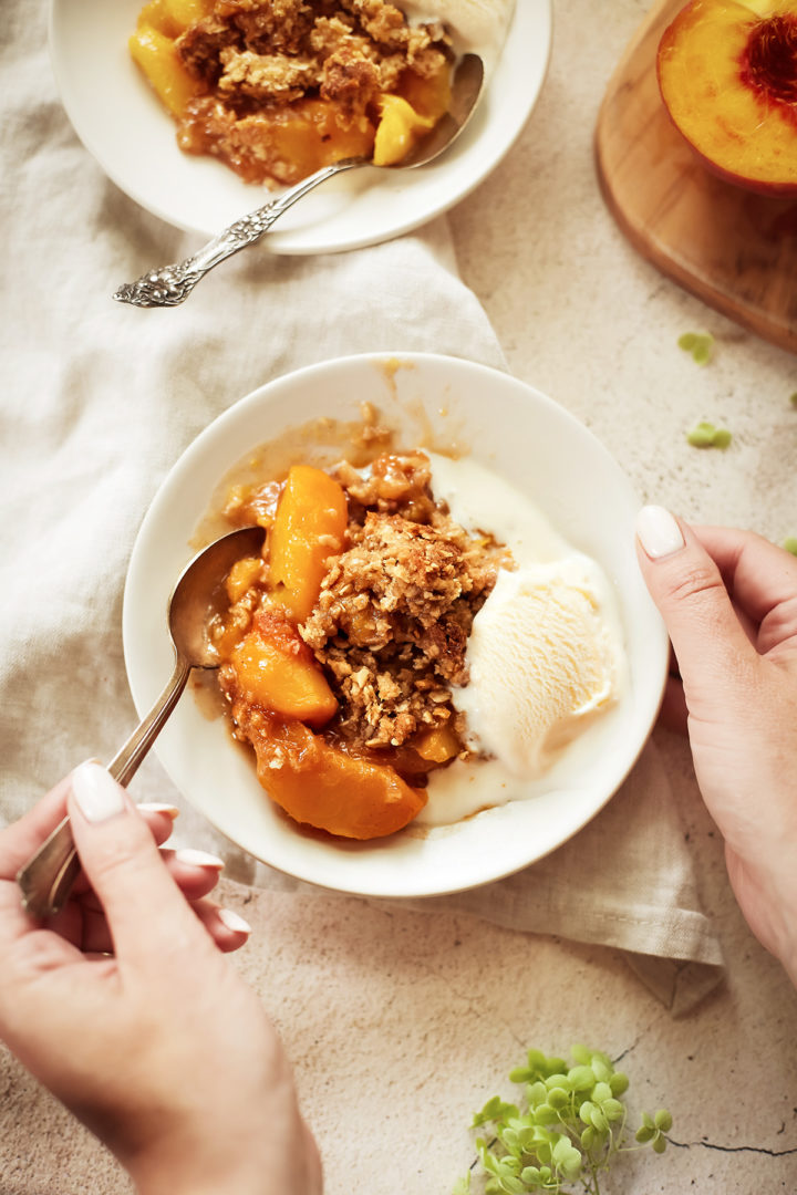 woman eating a bowl of peach crisp with oats topped with vanilla ice cream