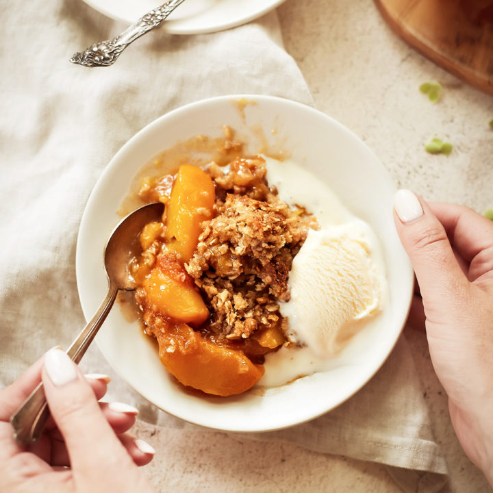 woman eating a bowl of easy peach crisp with vanilla ice cream