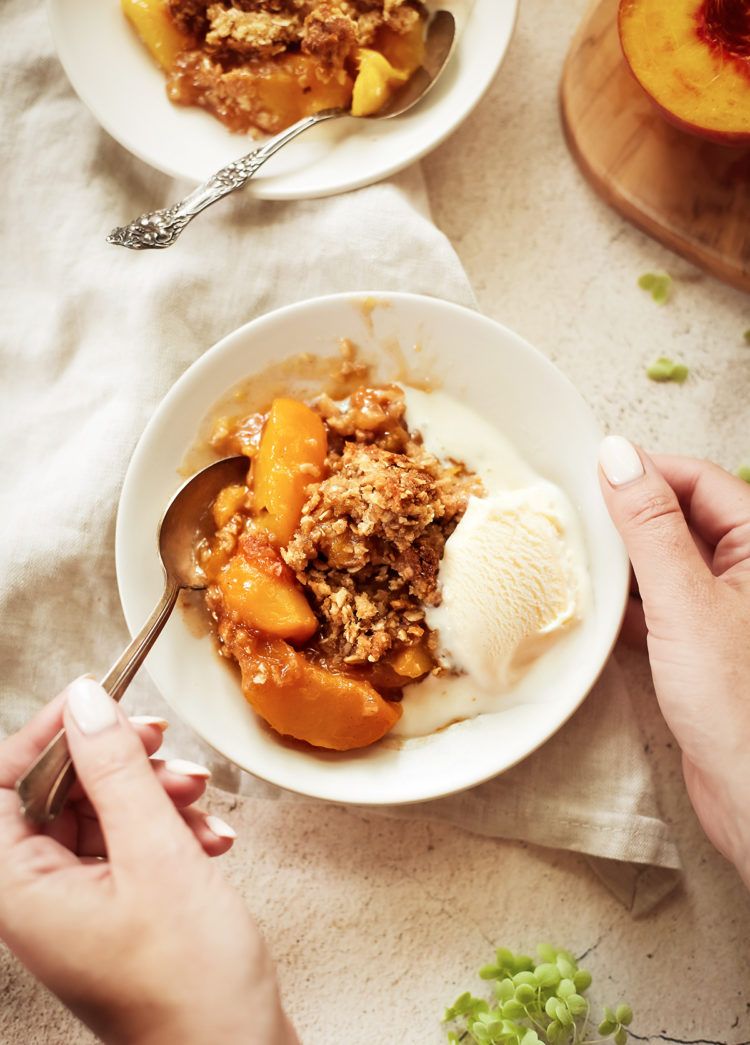 woman eating a bowl of easy peach crisp with vanilla ice cream