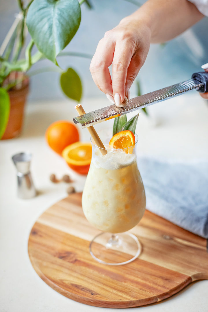 woman garnishing a painkiller recipe with fresh nutmeg