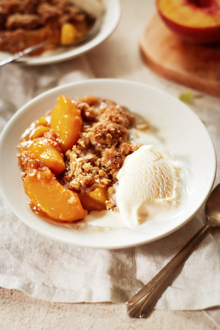 close up of peach oat crisp on a white plate with a scoop of vanilla ice cream