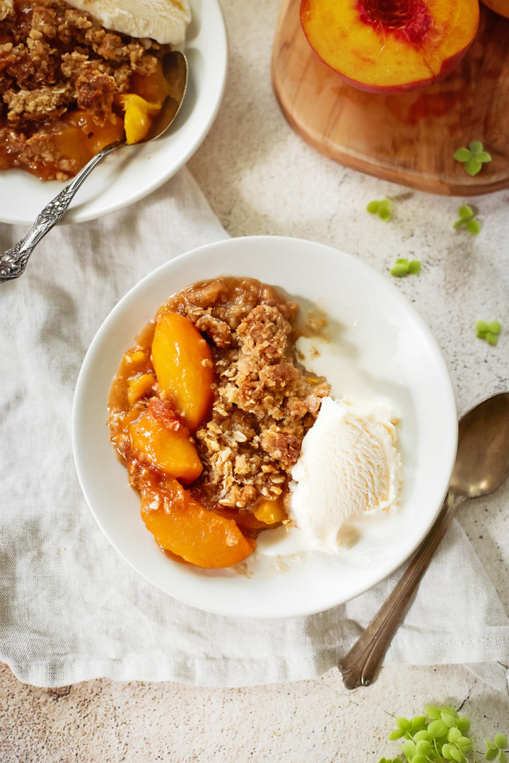 peach crisp with oatmeal topping on a plate with vanilla ice cream