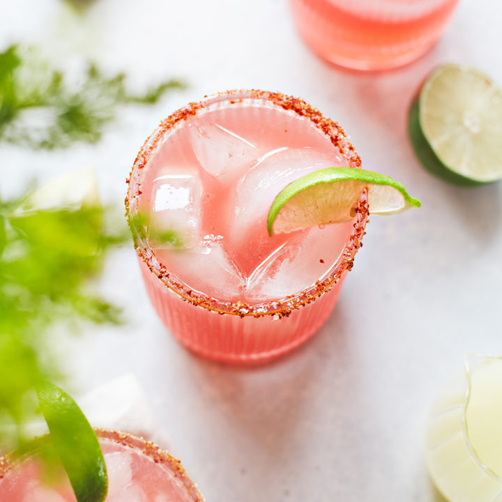 three glasses of watermelon margarita with a spicy salt rim and lime garnishes