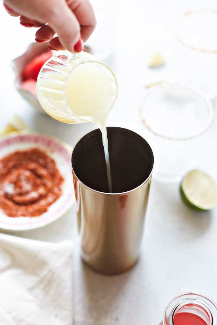 woman adding lime juice to a cocktail shaker with ingredients for a watermelon margarita