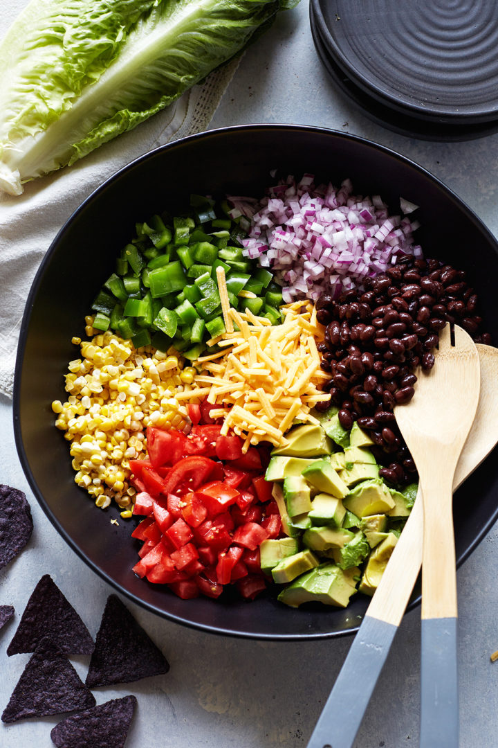 ingredients needed to make a veggie taco salad in a black bowl