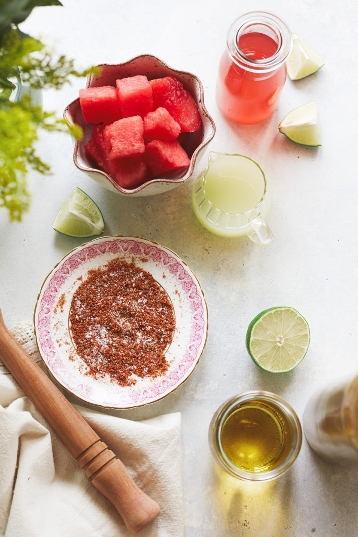 ingredients needed to make fresh watermelon margarita arranged in various dishes on a light surface