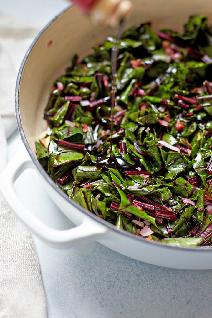 woman adding balsamic vinegar to cooked beet greens