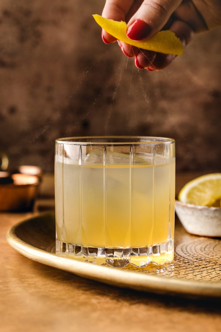 woman squeezing lemon over a glass of gold rush cocktail