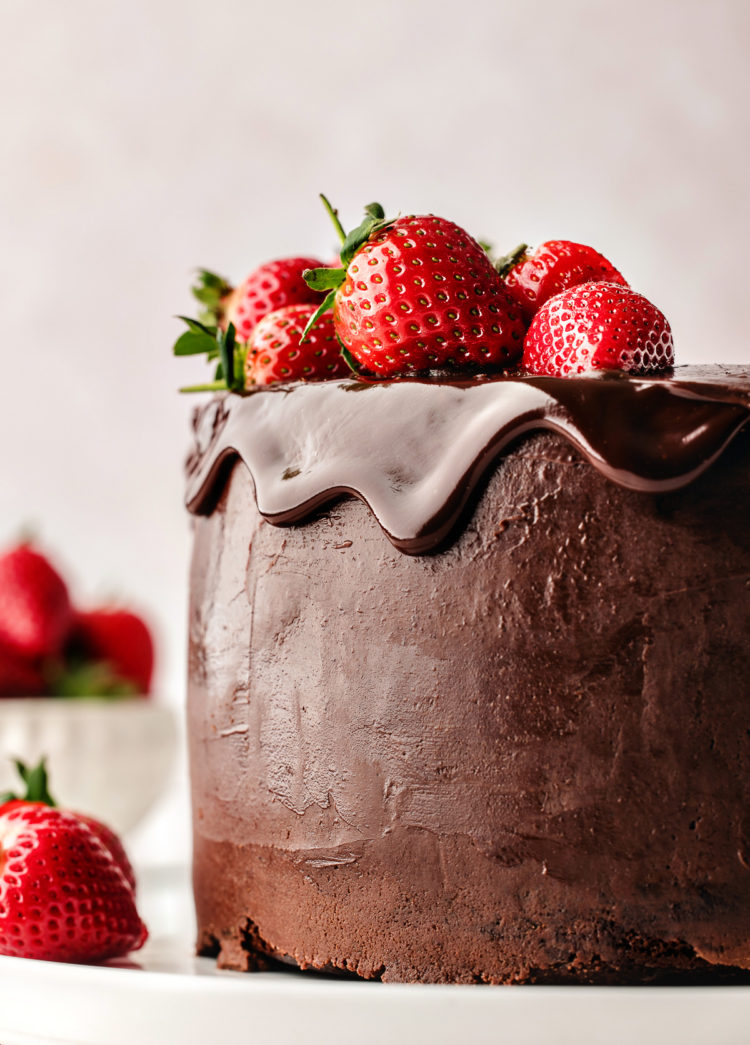 chocolate ganache cake on a white plate garnished with fresh strawberries