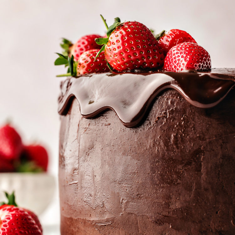 chocolate ganache cake on a white plate garnished with fresh strawberries