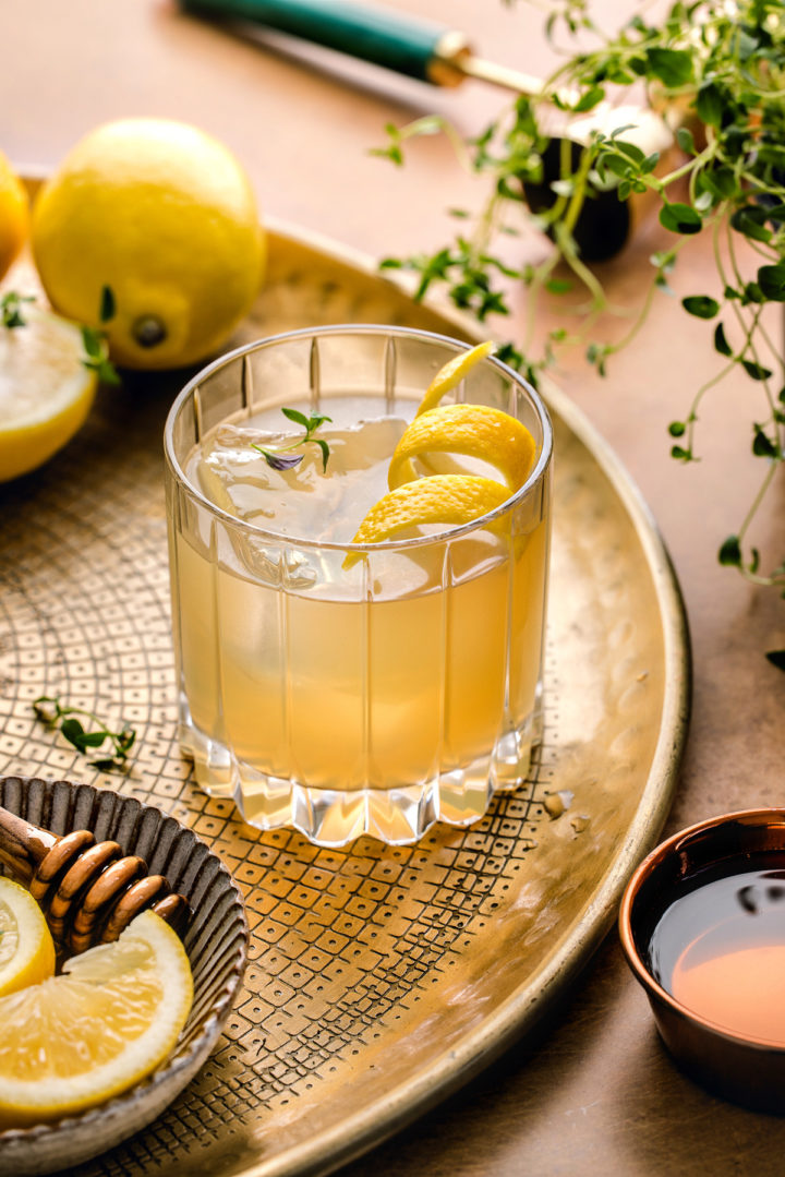 gold rush cocktail on a gold serving platter garnished with lemon and thyme