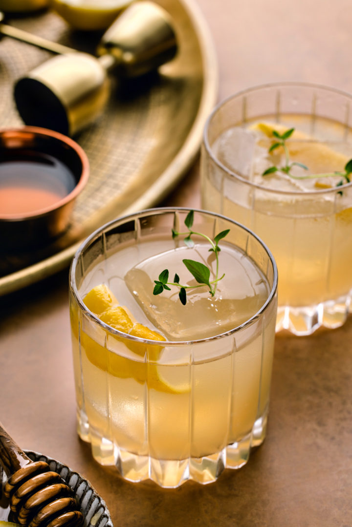 two glasses of bourbon gold rush cocktail garnished with lemon twists and fresh thyme