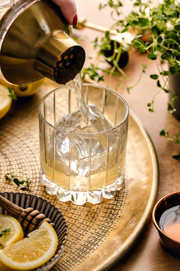 woman pouring a gold rush cocktail over ice in a glass