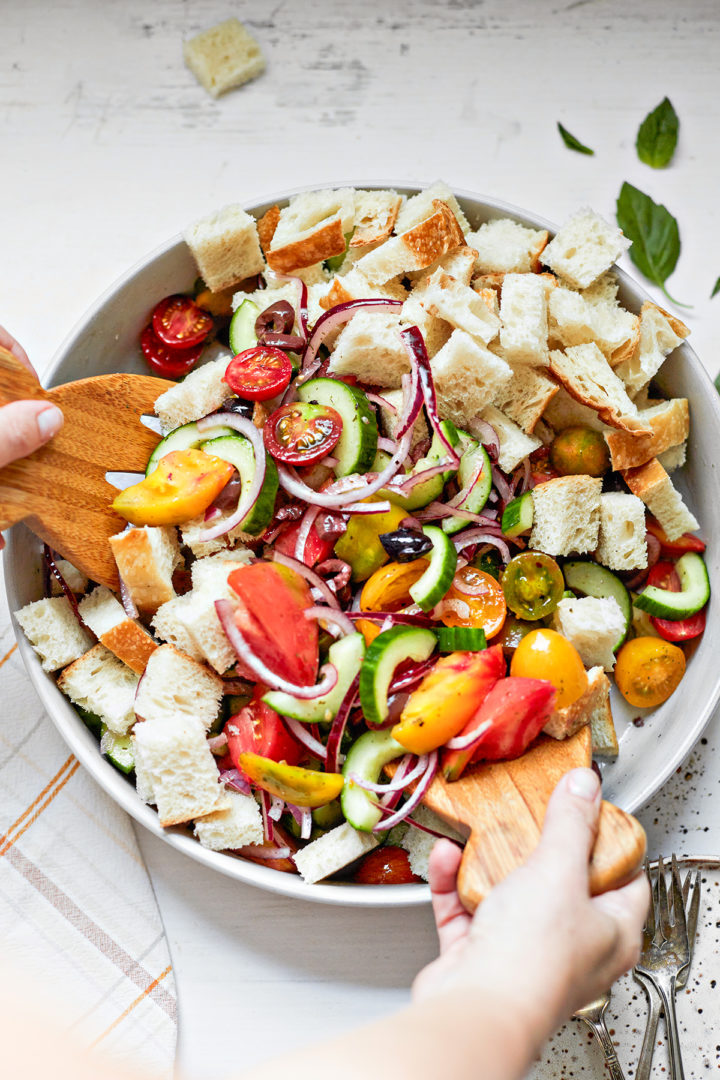 woman mixing a tomato bread salad with wooden salad tongs