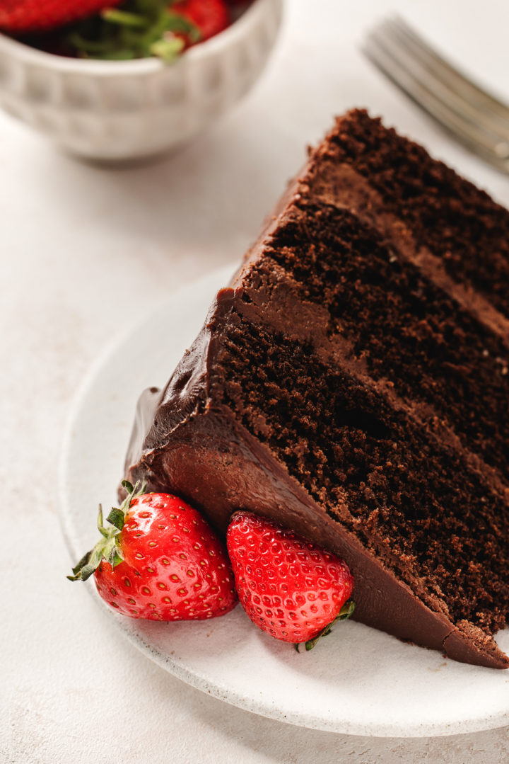 a slice of chocolate cake with ganache frosting and fresh strawberries on a white plate