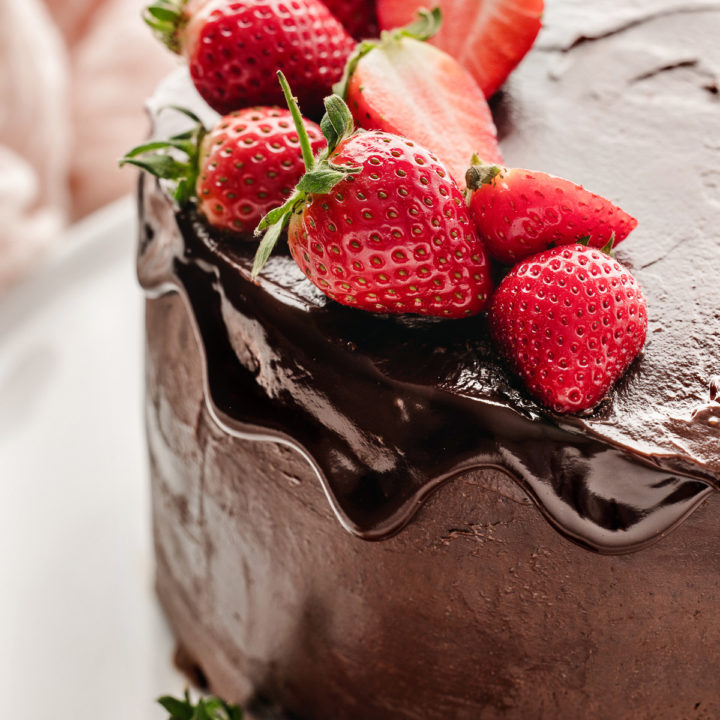 chocolate ganache cake on a white plate garnished with fresh strawberries