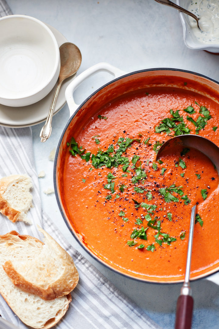 a pot of red pepper soup next to slices of bread