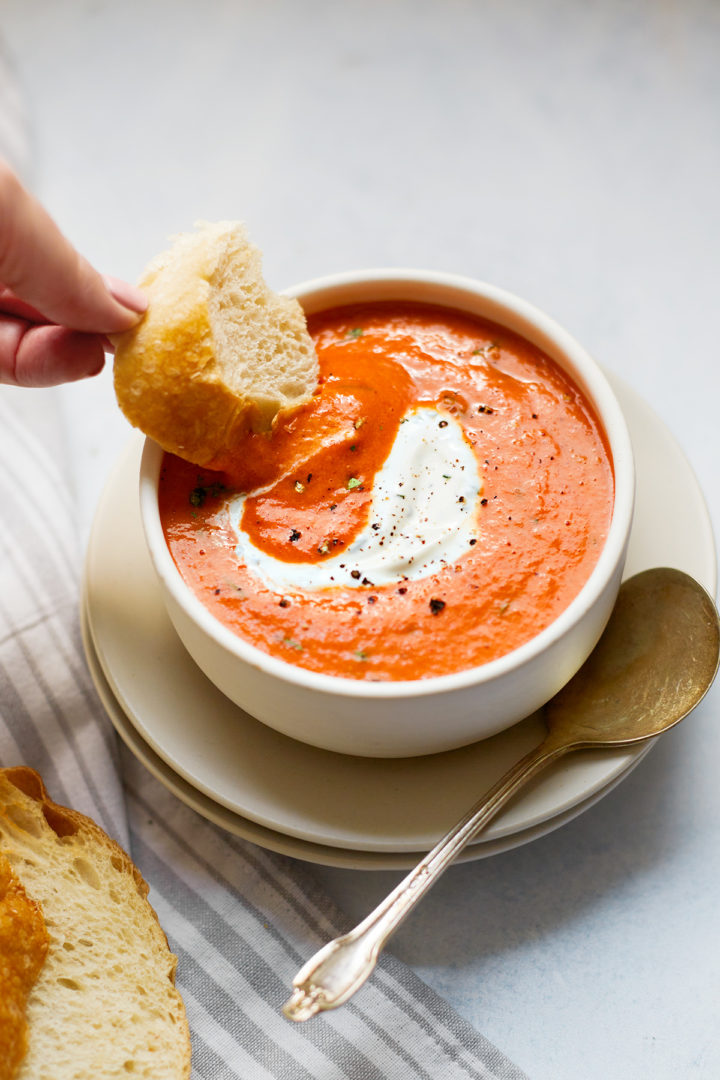 woman dipping bread in a bowl of roasted pepper soup