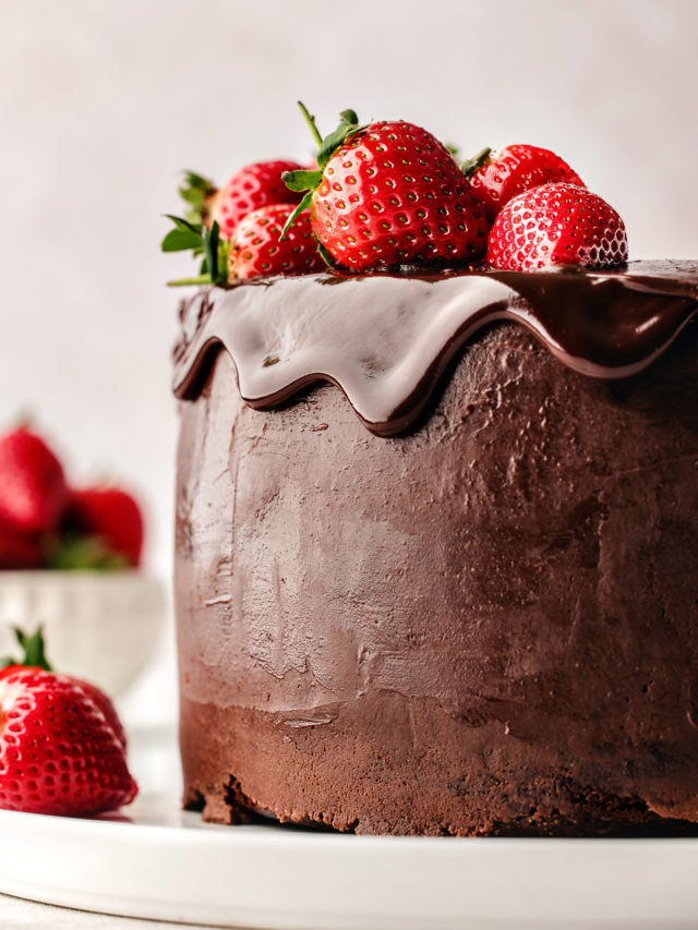 chocolate ganache cake on a white plate garnished with fresh strawberries