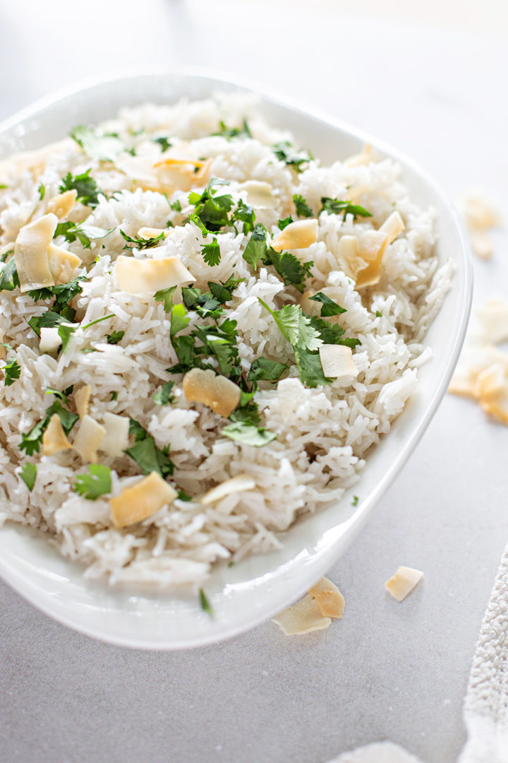 a white serving dish containing coconut rice topped with a toasted coconut garnish