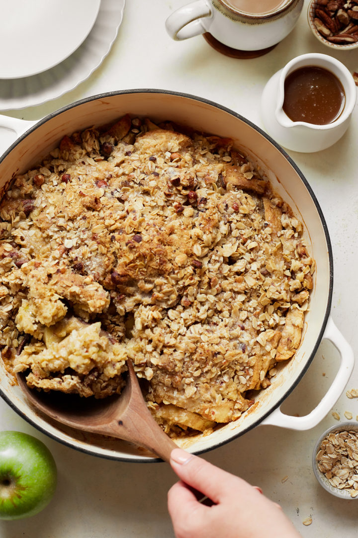 woman serving caramel apple crisp with a wooden spoon