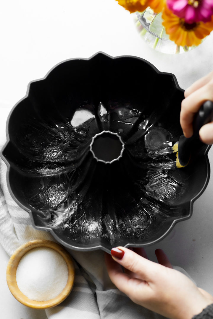 woman brushing shortening inside a bundt pan to grease it