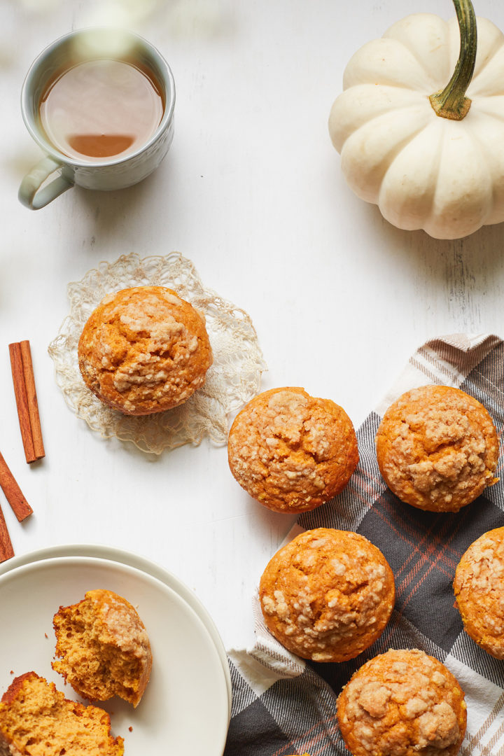 overhead photo of protein pumpkin muffins on a white surface with a cup of coffee and a white pumpkin