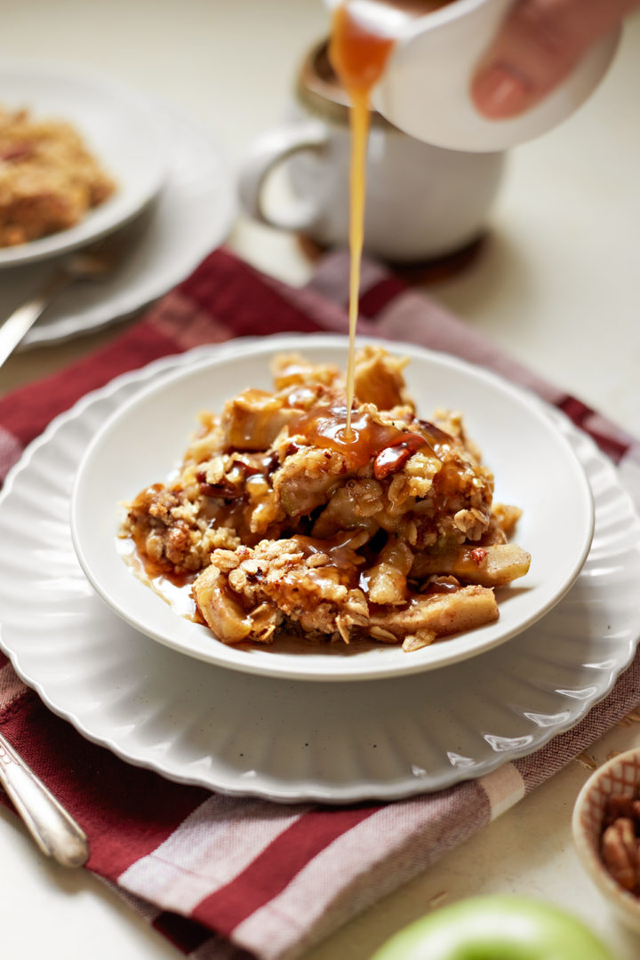 woman drizzling caramel sauce on a serving of caramel apple crisp