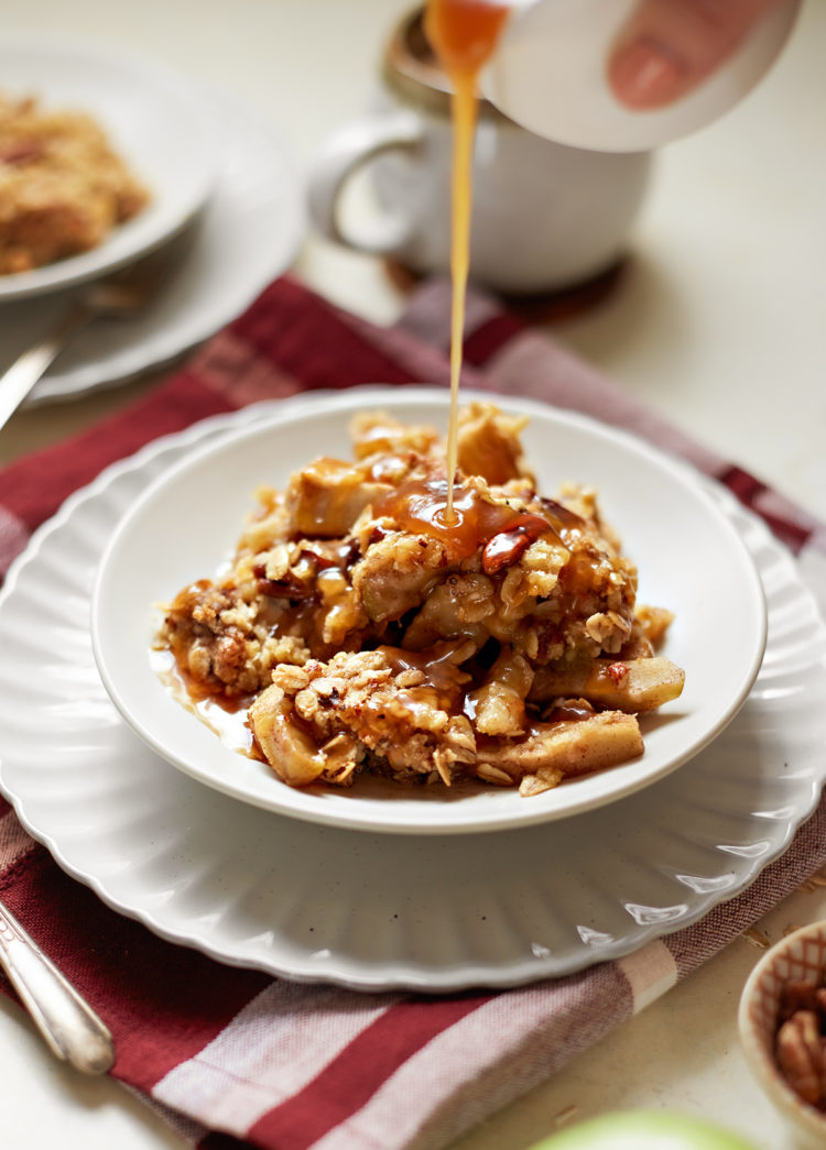 caramel drizzling over top of caramel apple crisp on a white plate