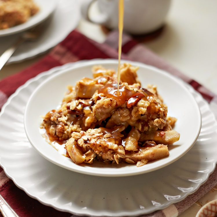 caramel drizzling over top of caramel apple crisp on a white plate