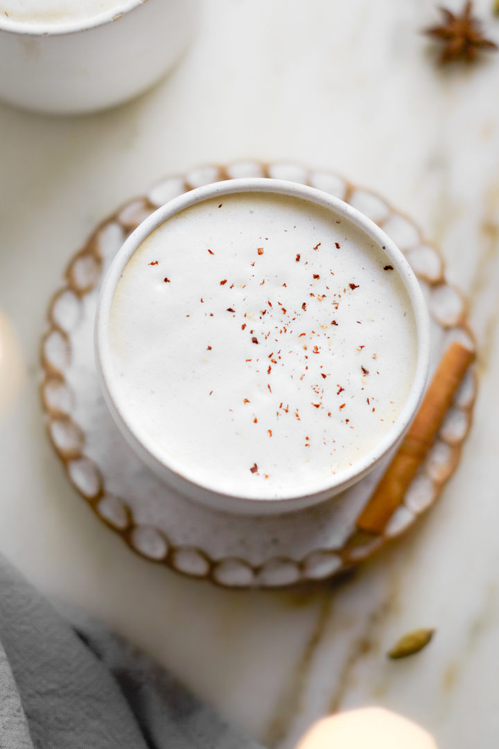 a mug of chai latte on a small plate with a cinnamon stick