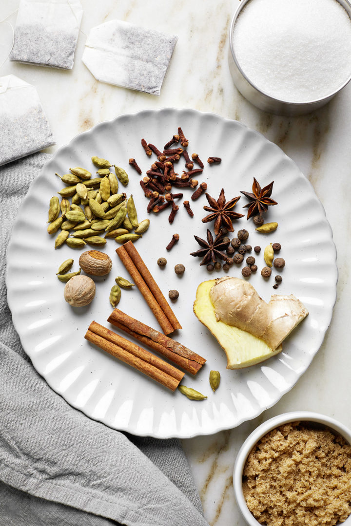 whole spices needed to make chai simple syrup on a white plate next to bowls of sugar