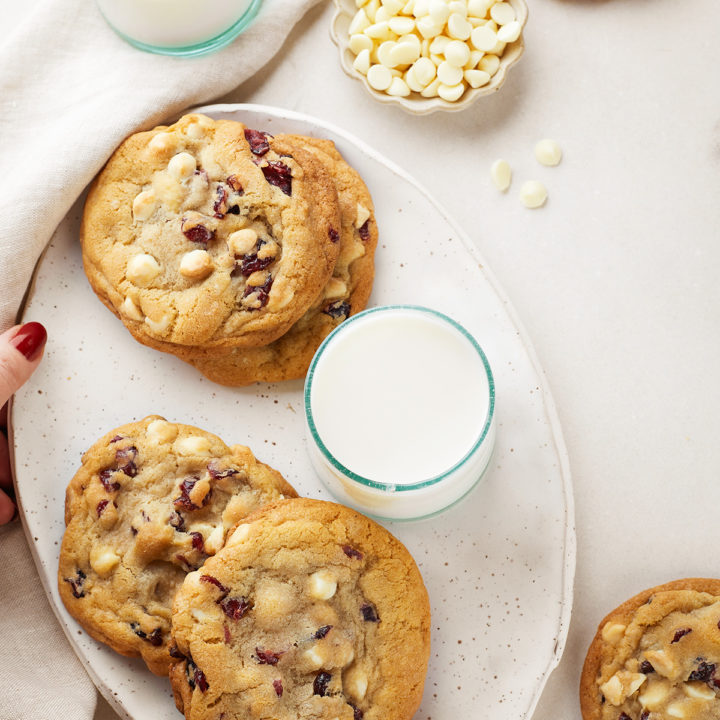 a plate of cranberry white chocolate cookies next to glasses of milk