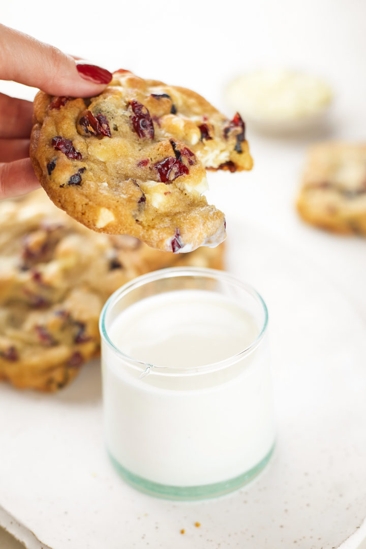 woman dipping a white chocolate dried cranberry cookie in a glass of milk