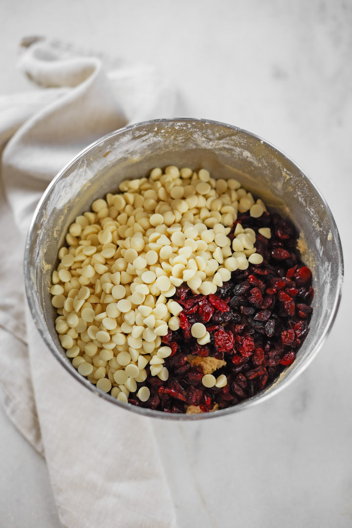 a bowl of cookie dough with white chocolate chips and cranberries