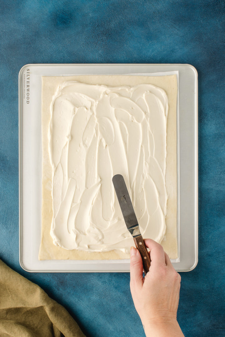 woman spreading cream cheese mixture on a puff pastry