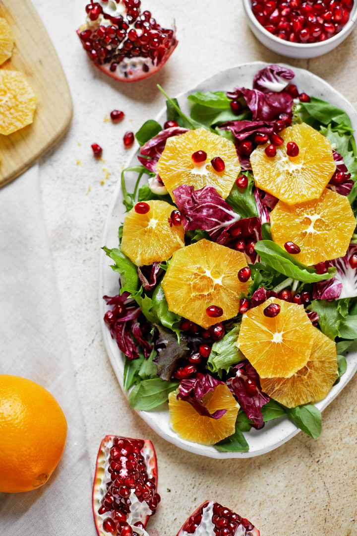 a platter of mixed greens and arugula topped with orange slices and pomegranate