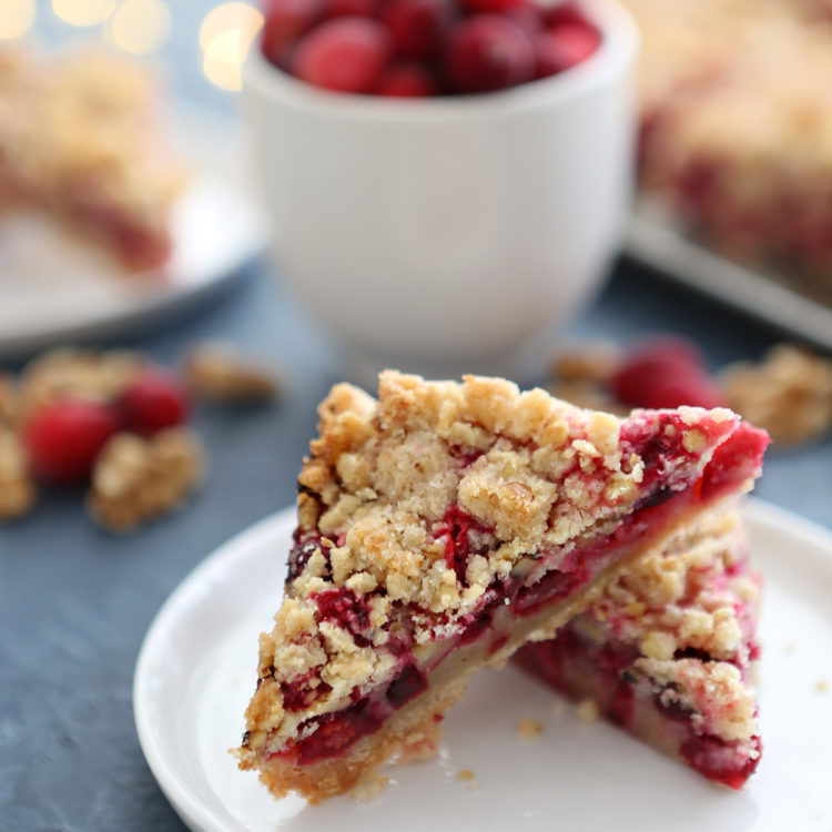 cranberry walnut bars on a white plate surrounded by christmas lights