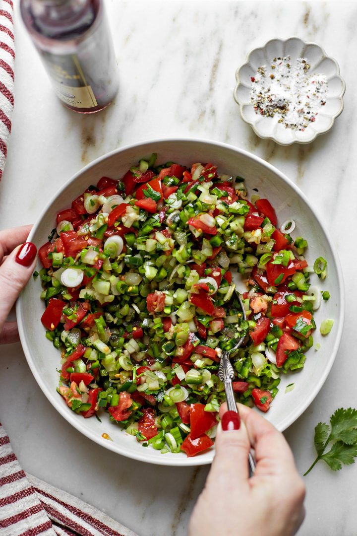 woman mixing chopped vegetables in a white bowl