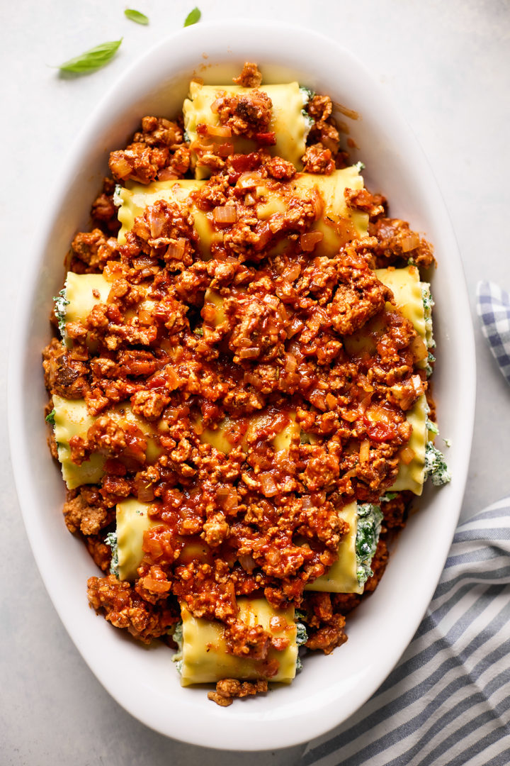 A white baking dish filled with sausage lasagna rolls, topped with a rich, meaty marinara sauce before adding cheese