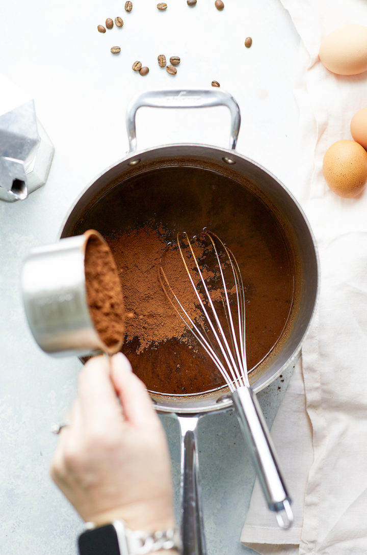 woman adding cocoa powder to a saucepan with melted butter and sugar