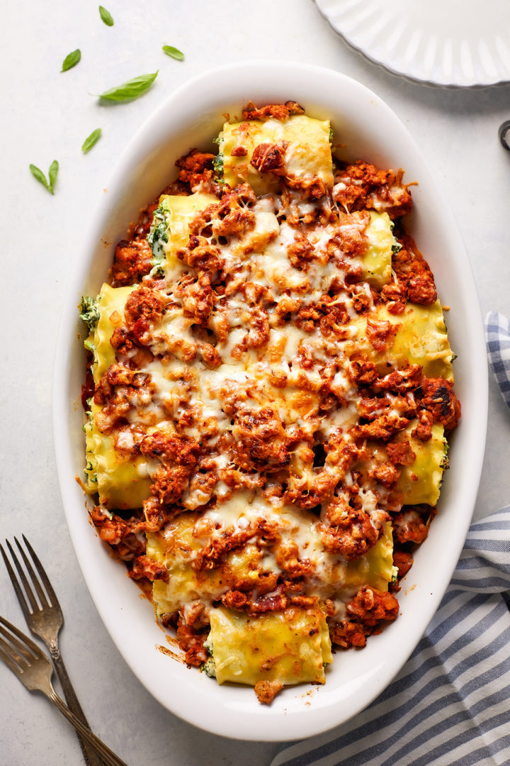 A white baking dish filled with sausage lasagna rolls, topped with a rich, meaty marinara sauce and melted cheese, ready to be served.