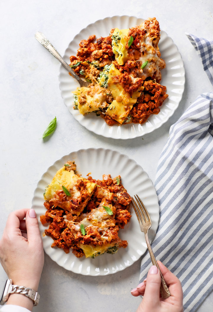 A woman holding a fork, about to take a bite of sausage lasagna rolls served on a white plate, with melted cheese and hearty meat sauce  