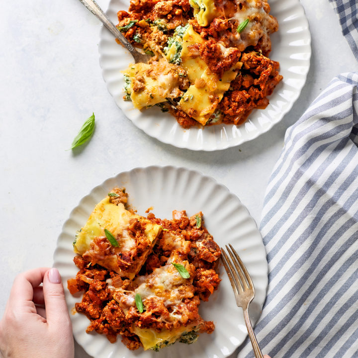 A woman holding a fork, about to take a bite of sausage lasagna rolls served on a white plate, with melted cheese and hearty sausage meat sauce