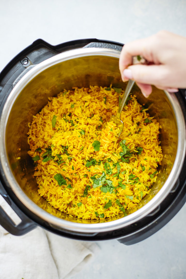 A woman fluffing freshly cooked turmeric yellow rice in an Instant Pot,  