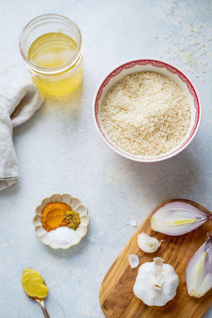 Ingredients for turmeric yellow rice, including basmati rice, spices, chicken stock, and aromatics, neatly arranged for preparing a turmeric rice recipe.