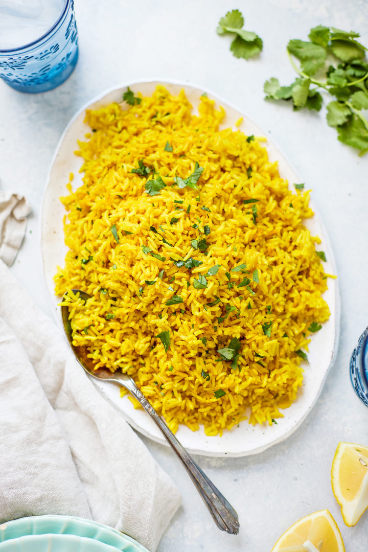 A plate of Instant Pot turmeric rice garnished with fresh cilantro, served with a spoon, lemon wedges, and fresh herbs. 