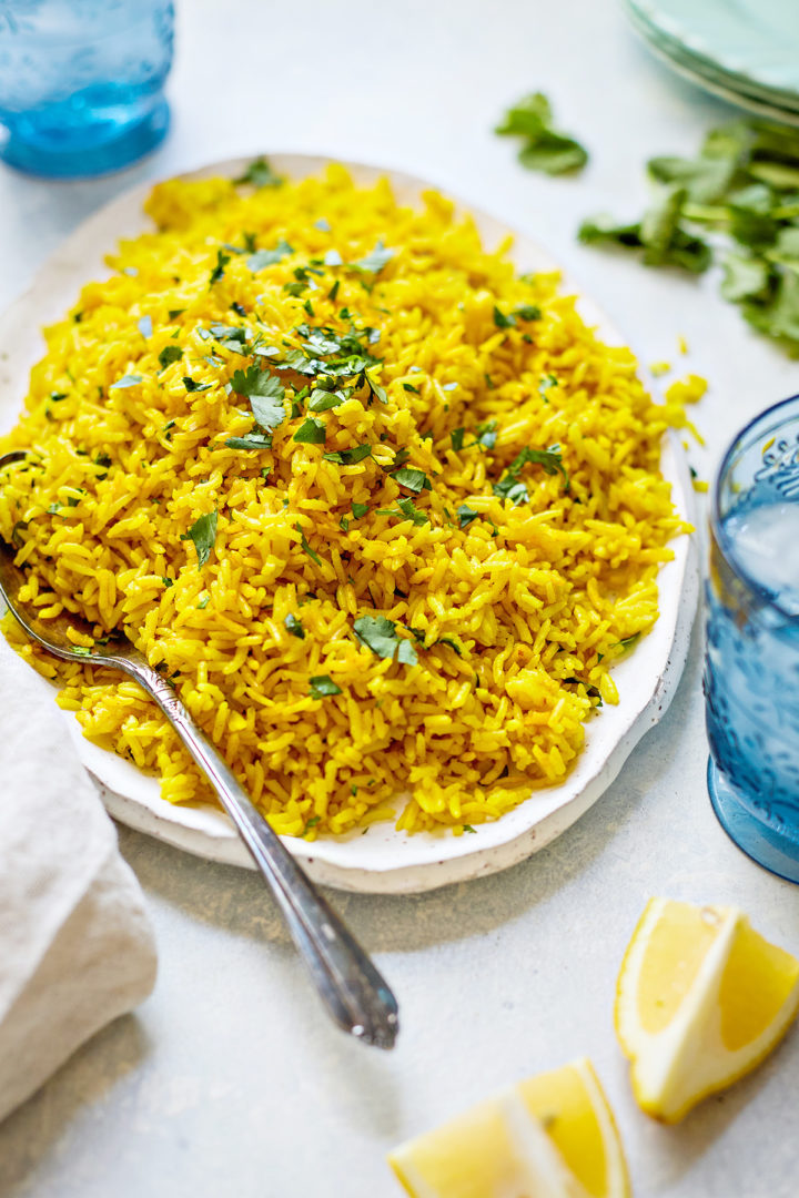 A plate of Instant Pot turmeric rice served with fresh cilantro, lemon, and a spoon, beautifully styled on a light blue background.